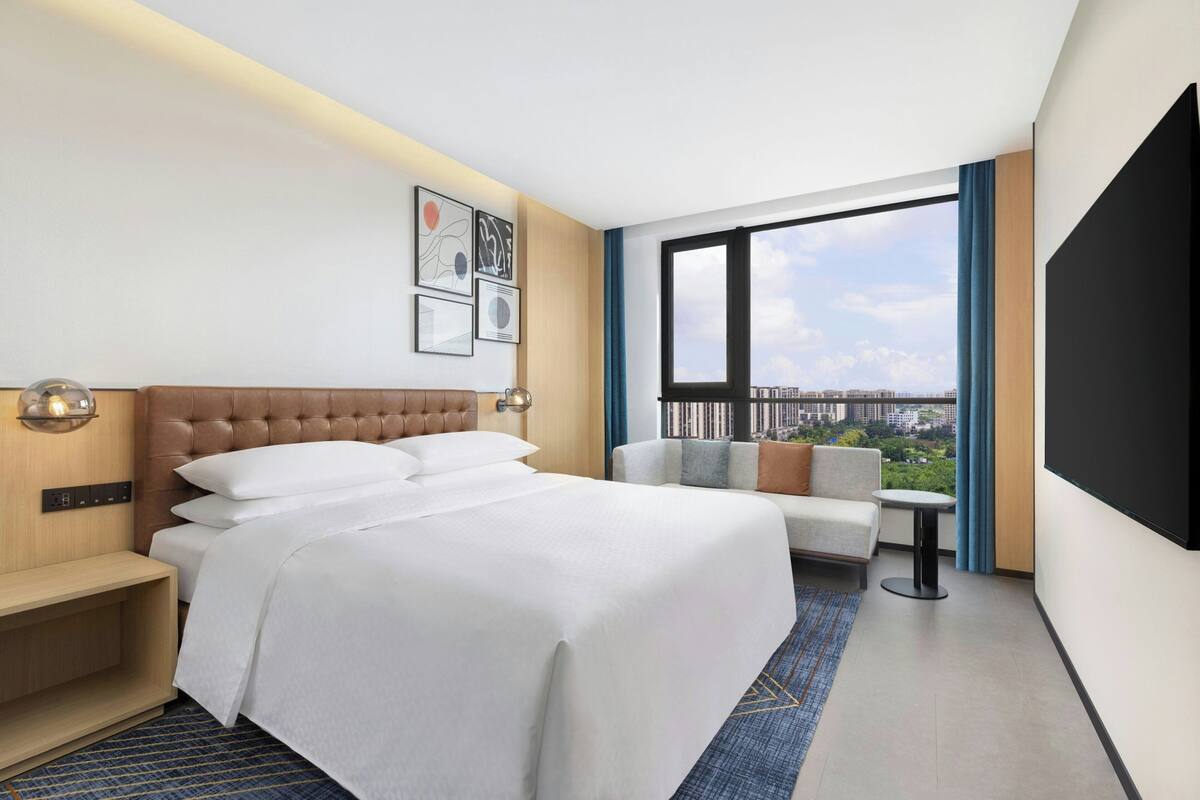 A hotel room with a large bed, a sofa, a TV, and a city view.