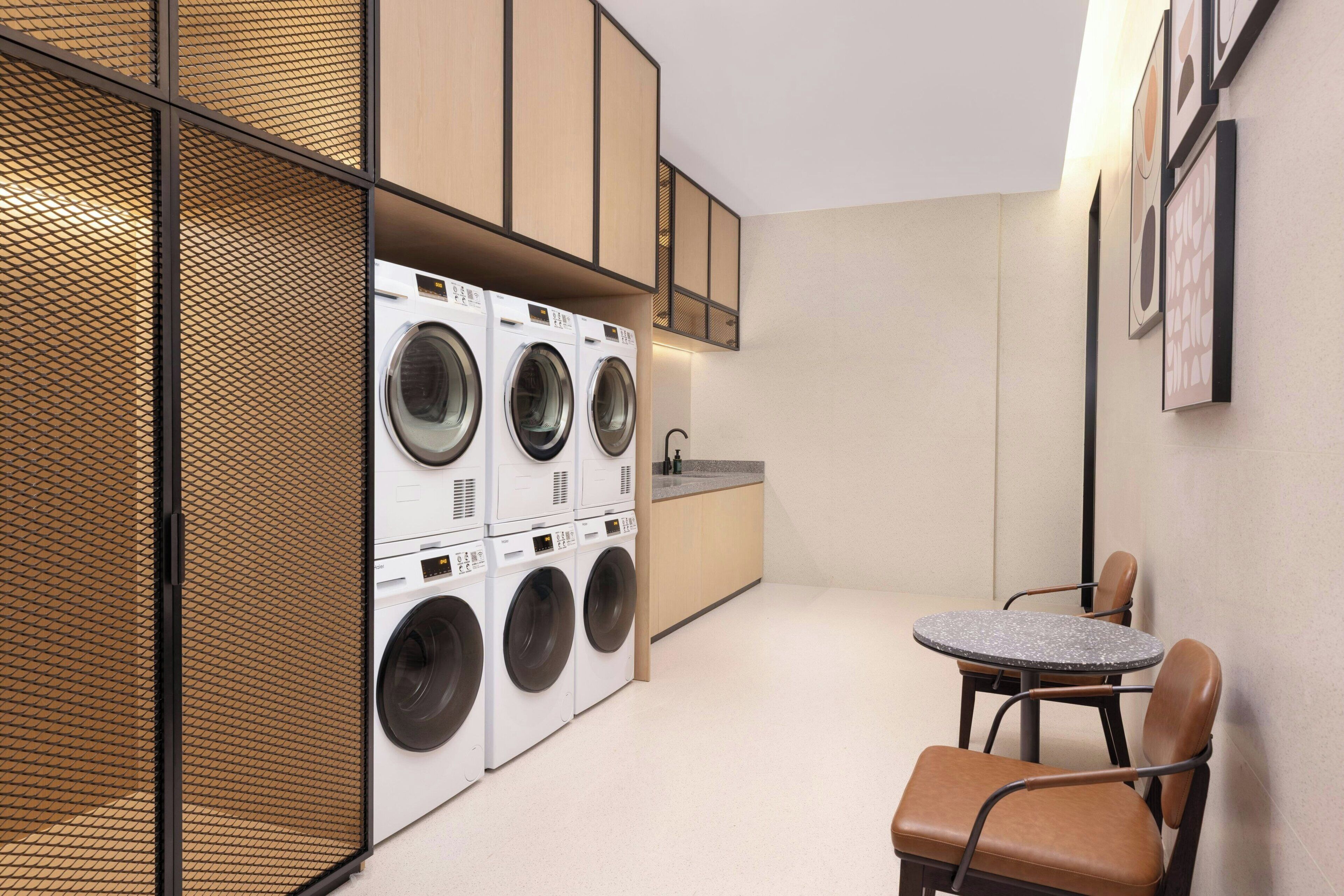 A compact laundry room with a washing machine, a sink, and a small table with chairs.