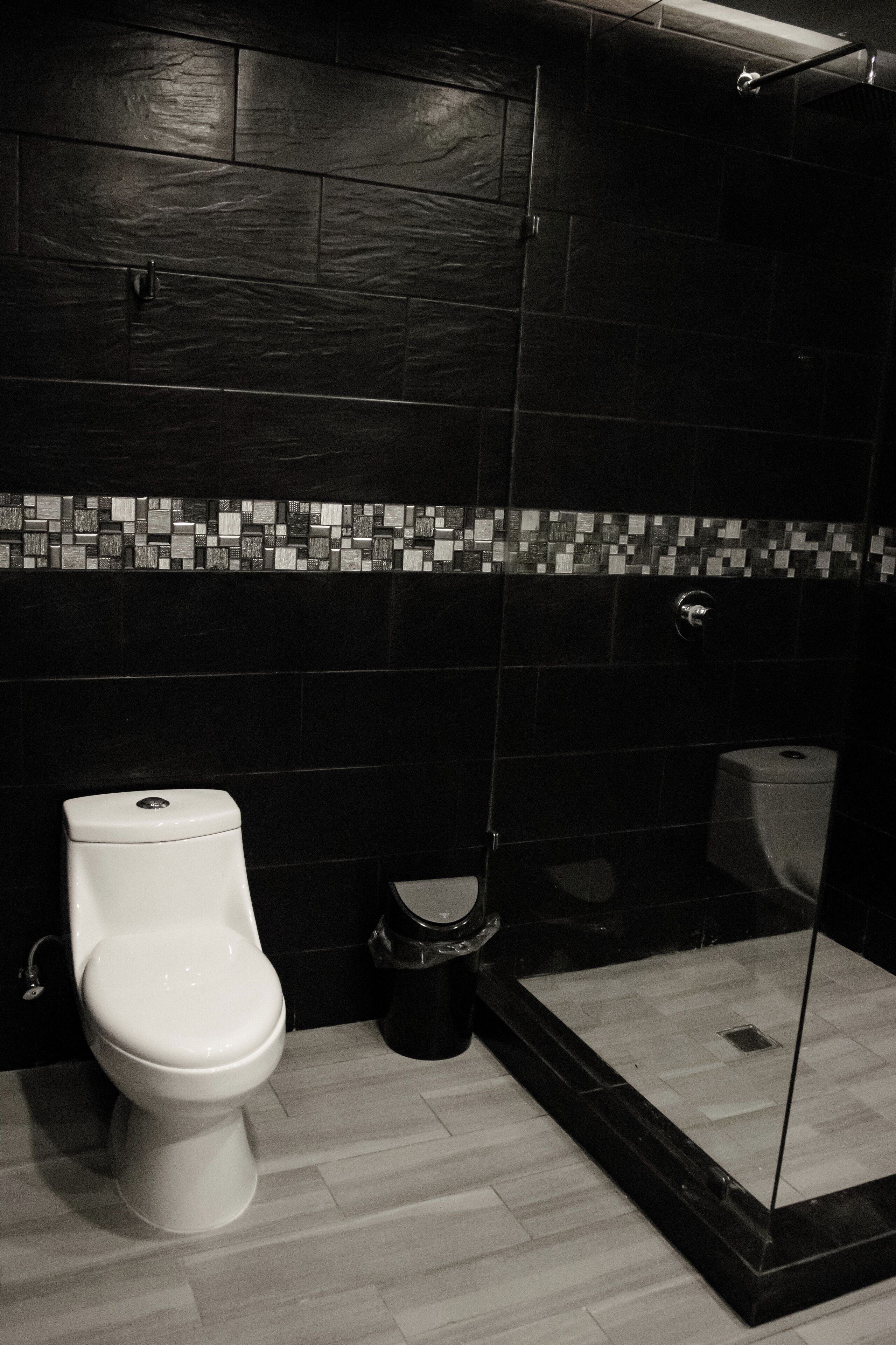 A bathroom with a white toilet, a trash bin, and a glass-enclosed shower area.