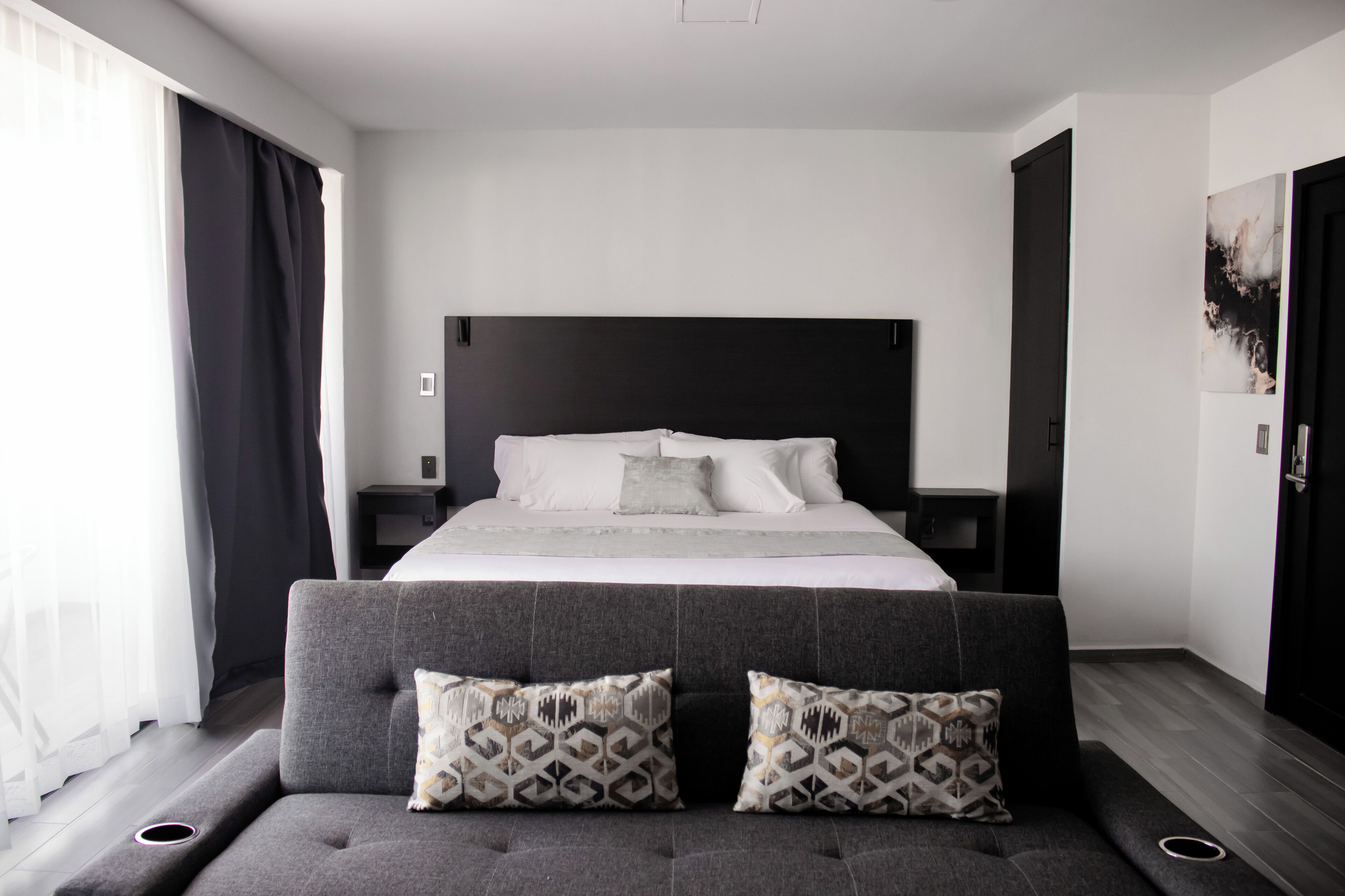 A modern bedroom with a large bed, grey upholstered sofa, and a black headboard.