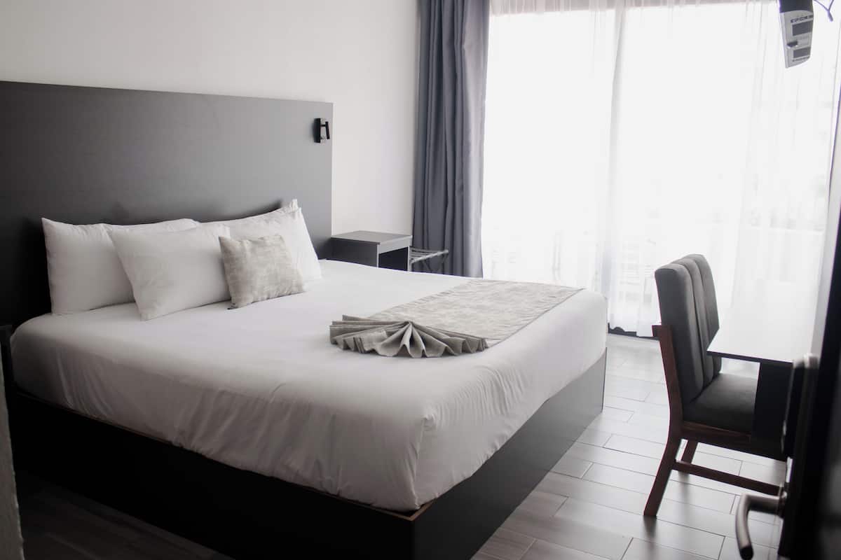 Une chambre d’hôtel moderne avec un grand lit, une table de chevet, une chaise et une vue sur l’extérieur par une fenêtre.