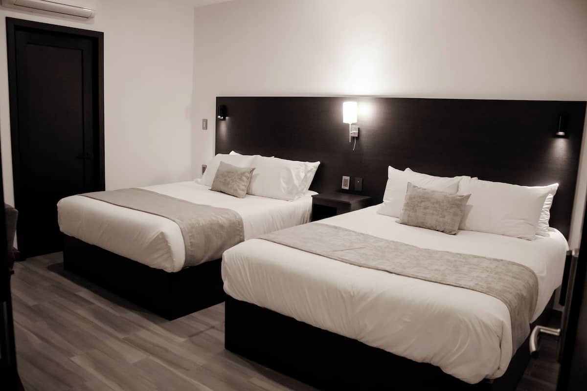 Une chambre d’hôtel avec deux lits, chacun doté de draps blancs et d’une tête de lit sombre.