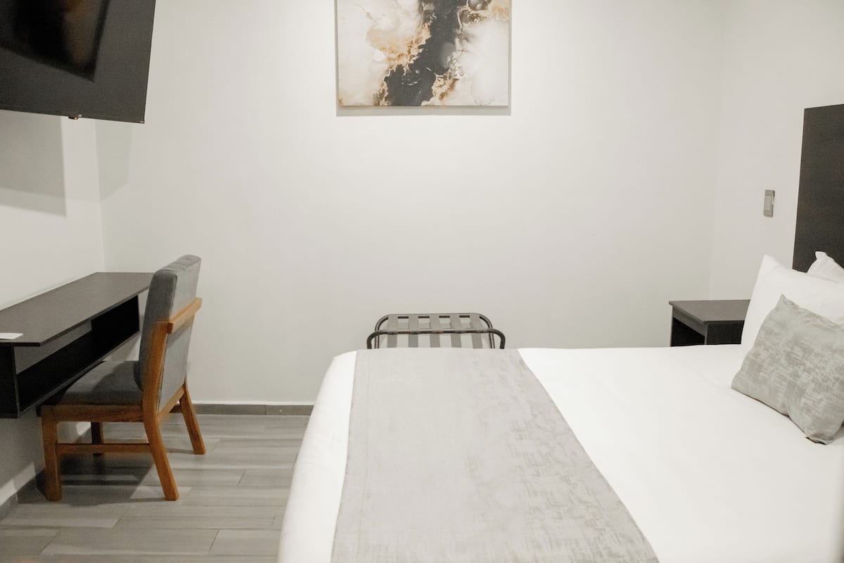 Une chambre d’hôtel avec un lit, un bureau, une chaise, un téléviseur fixé au mur et un tableau accroché au mur.