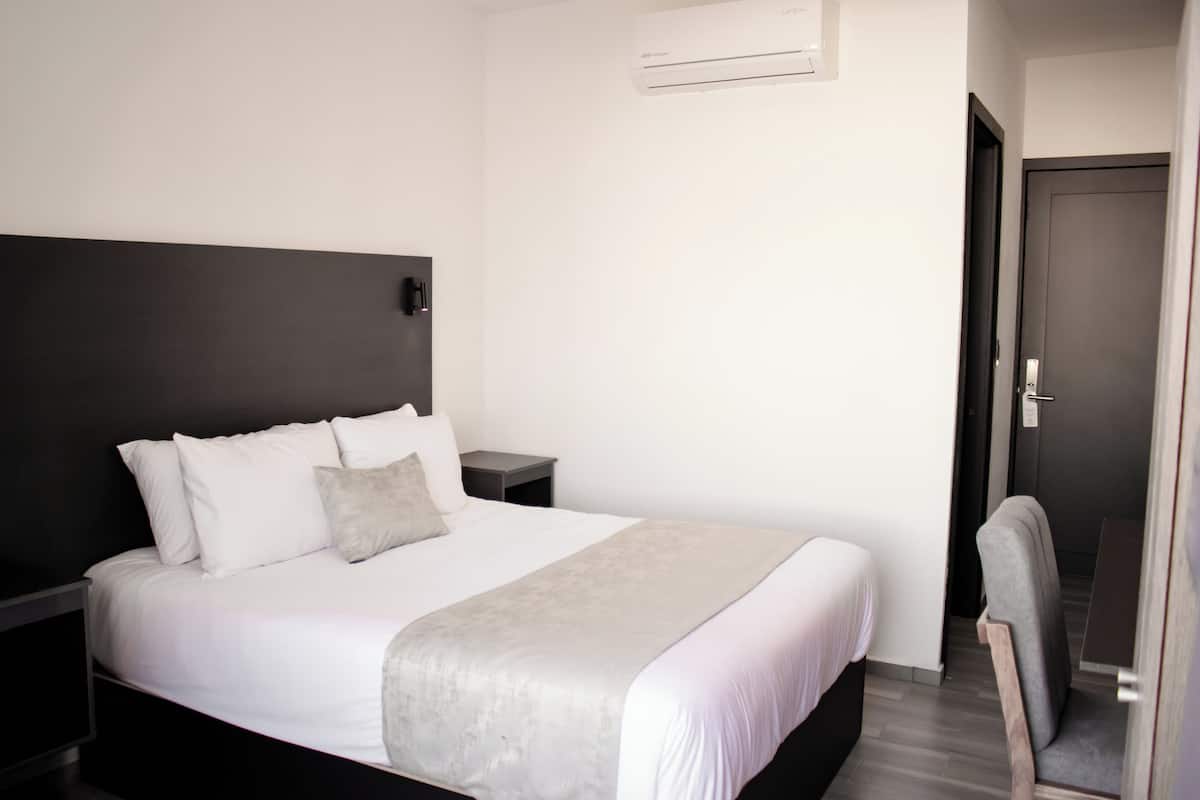 Une chambre d’hôtel avec un grand lit, une table de chevet, une chaise et une porte.