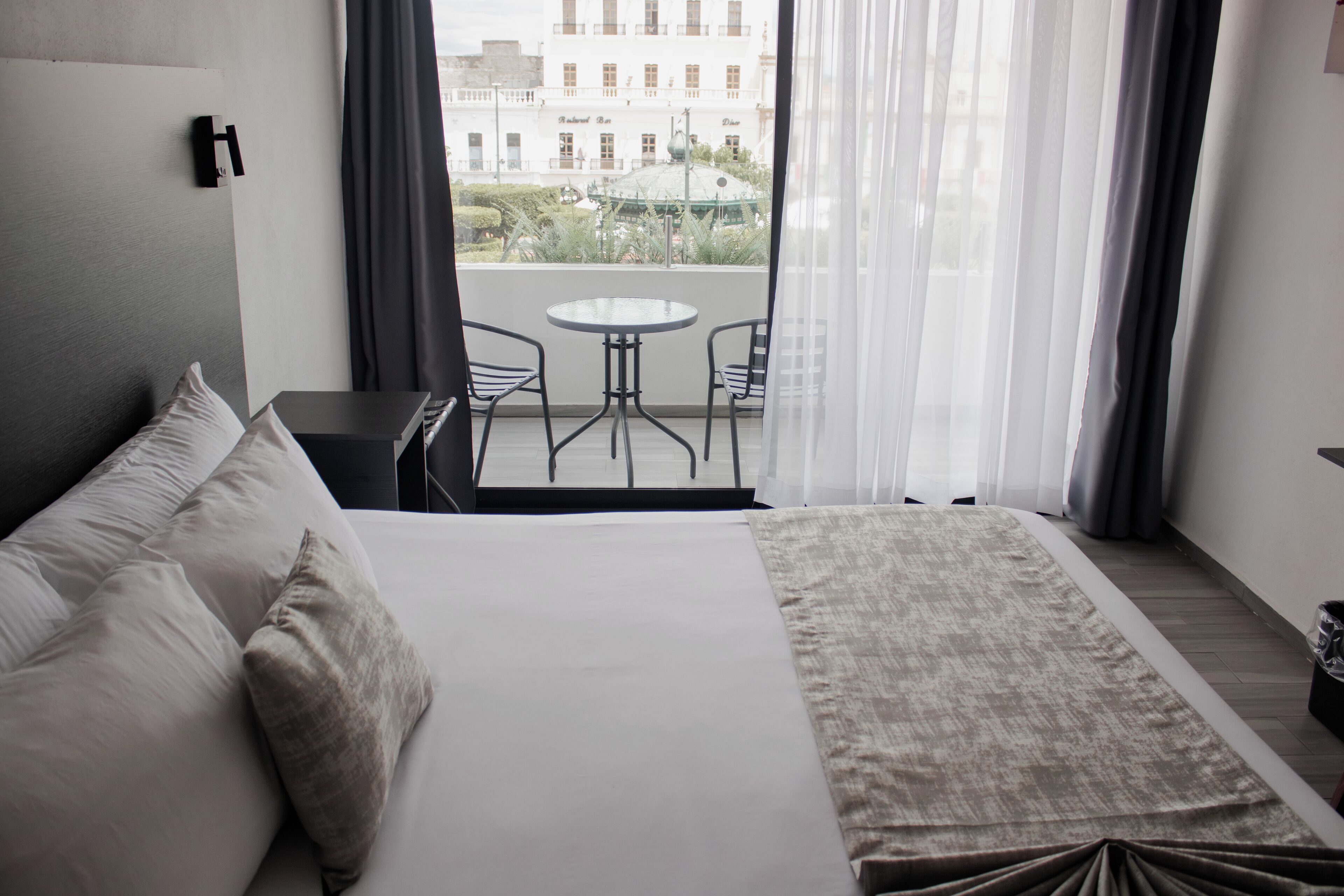 Une chambre d’hôtel avec un lit, une petite table et un balcon donnant sur des immeubles.