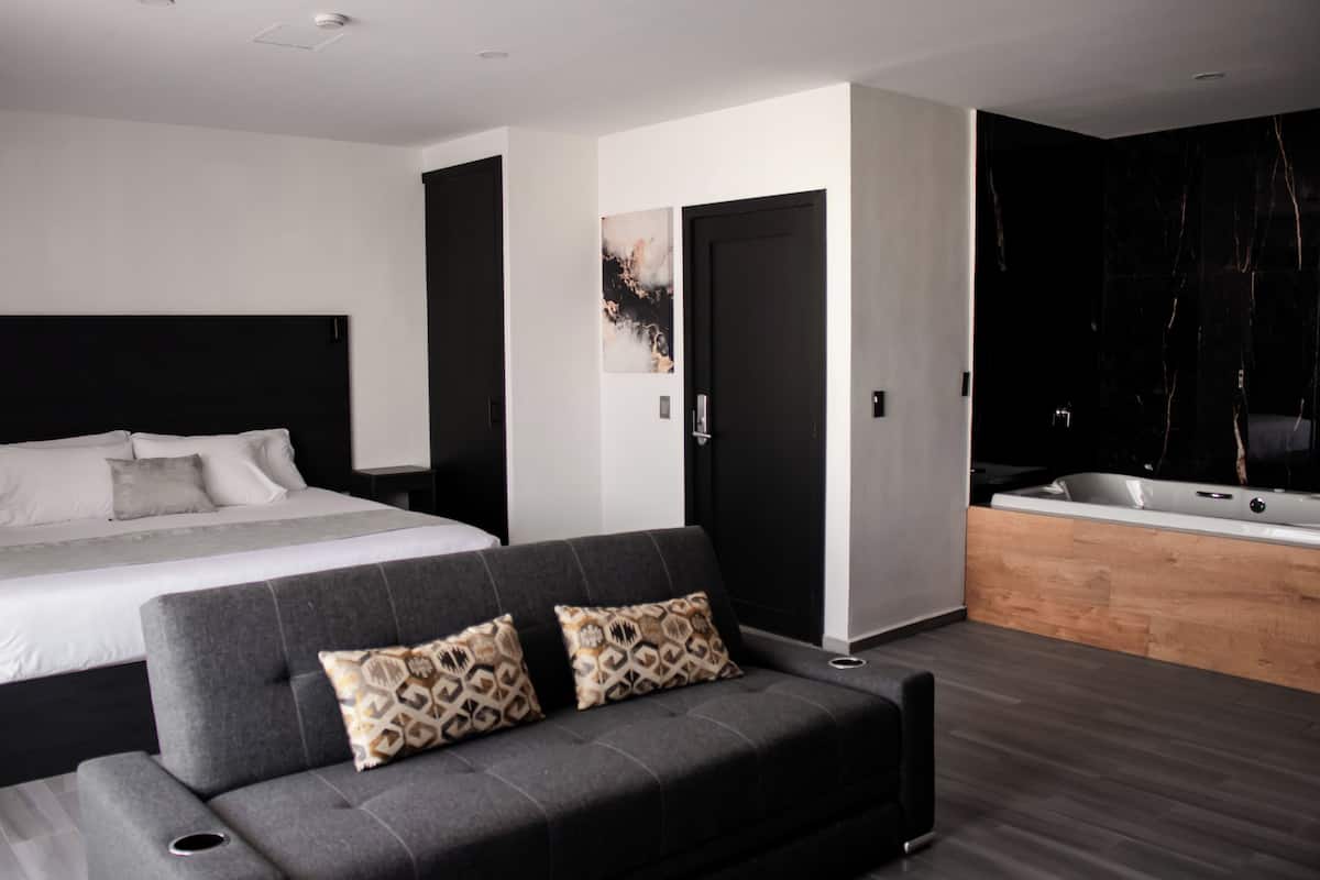 Une chambre moderne avec un grand lit, un canapé gris, une baignoire noire et un banc en bois.