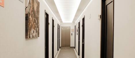 A long, narrow hallway with doors on both sides, a trash can on the left, and a ceiling light.