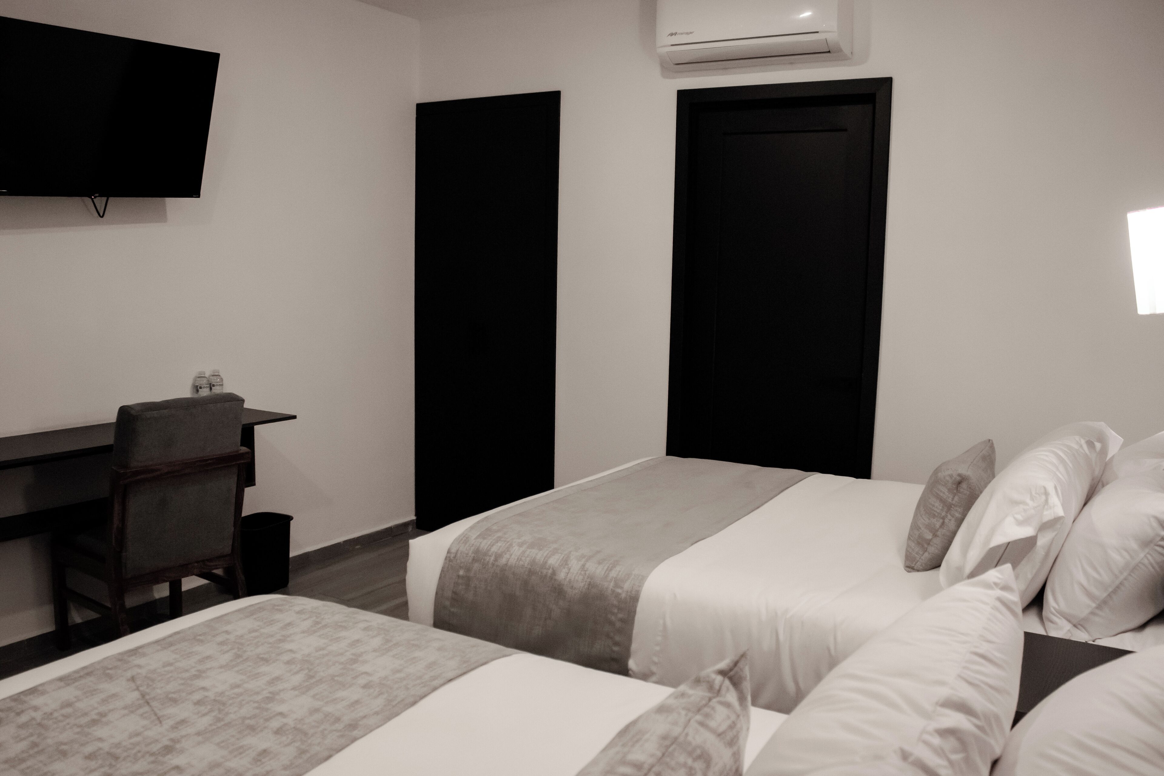 A hotel room with two beds, a desk, a chair, and a TV mounted on the wall.