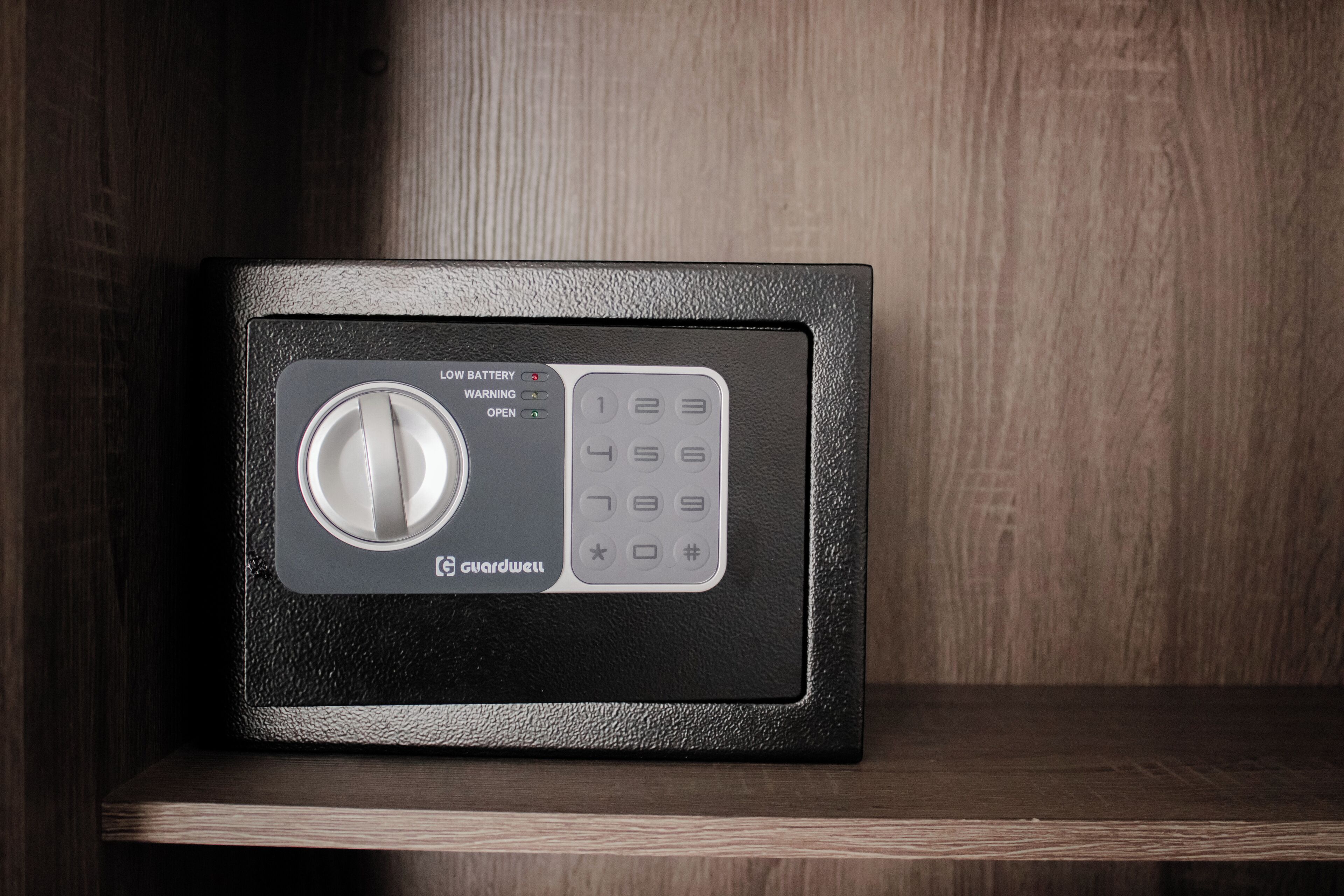 A black safe with a keypad and a dial lock, placed on a wooden shelf.