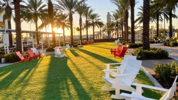 A well-maintained lawn with white lounge chairs and red chairs, surrounded by palm trees and a clear sky. - Enjoy our brand new home close to Hollywood in Hallandale Beach! (Hallandale Beach)