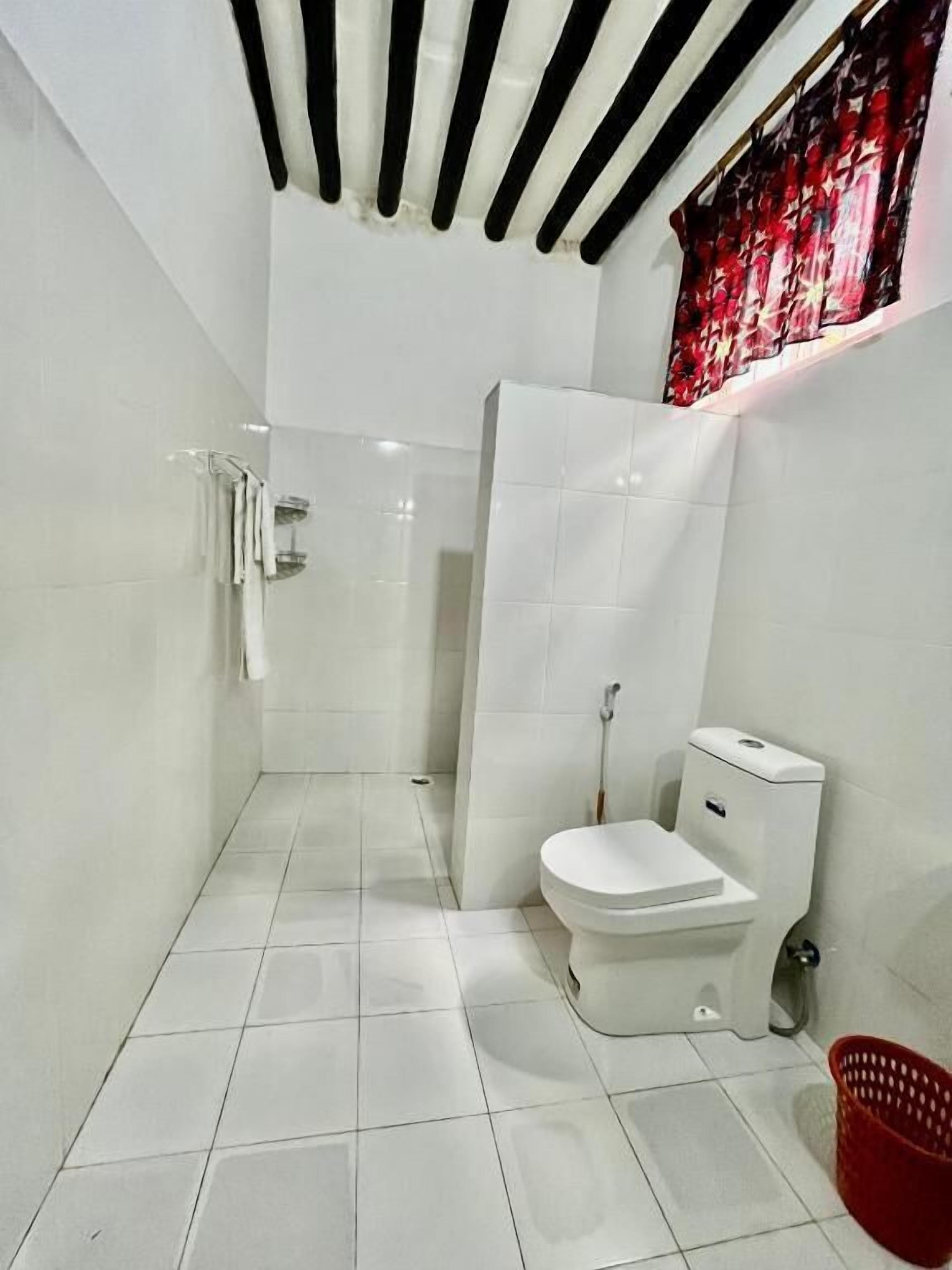 A modern bathroom with a toilet, shower, and a red basket on the floor.
