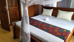Un dormitorio con una cama, dosel, cabecero de madera y una colcha colorida.