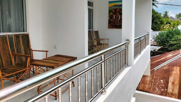 Un balcón con sillas de madera y barandilla de metal.