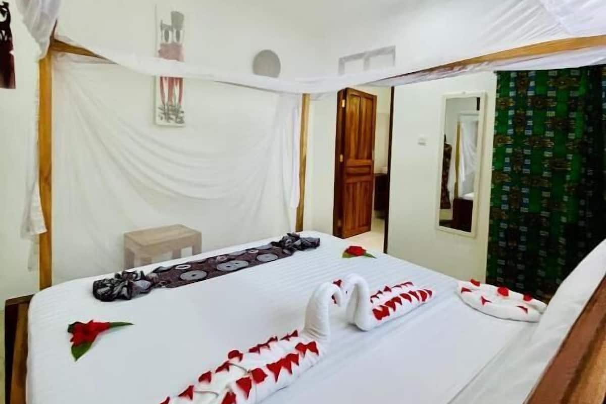 Una cama bien hecha con ropa de cama blanca y decoración de rosas rojas, un cabecero de madera y un espejo en la pared.