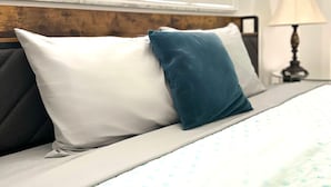 Un lit avec un oreiller blanc et bleu, une tête de lit en bois et une fenêtre avec des volets blancs.