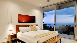 Ein Schlafzimmer mit einem großen Bett, einem Nachttisch, einer Bank, einem Gemälde und Meerblick.