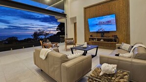 Ein modernes Wohnzimmer mit großem Fernseher, bequemen Sitzmöglichkeiten und Blick zum Himmel.