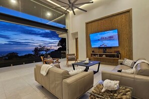 Ein modernes Wohnzimmer mit großem Fernseher, bequemen Sitzmöglichkeiten und Blick zum Himmel.