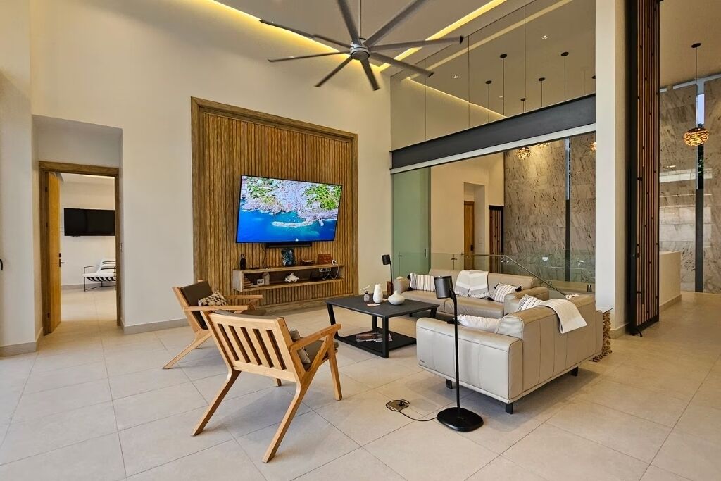 Ein modernes Wohnzimmer mit Fernseher, Sofa, Couchtisch und Holzstühlen.
