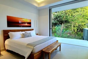 Ein Schlafzimmer mit einem großen Bett, einer Bank und Blick auf Grün hinter einer Schiebetür.
