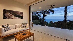 Ein modernes Wohnzimmer mit Sofa, Couchtisch und großem Fenster mit Meerblick.