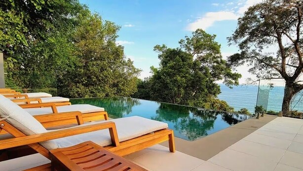 Ein Poolbereich mit Holzliegen und Blick aufs Meer.