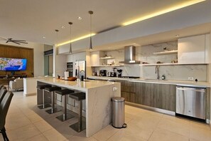 Una cucina moderna con isola centrale, sgabelli da bar, lavastoviglie in acciaio inossidabile e televisore a parete.