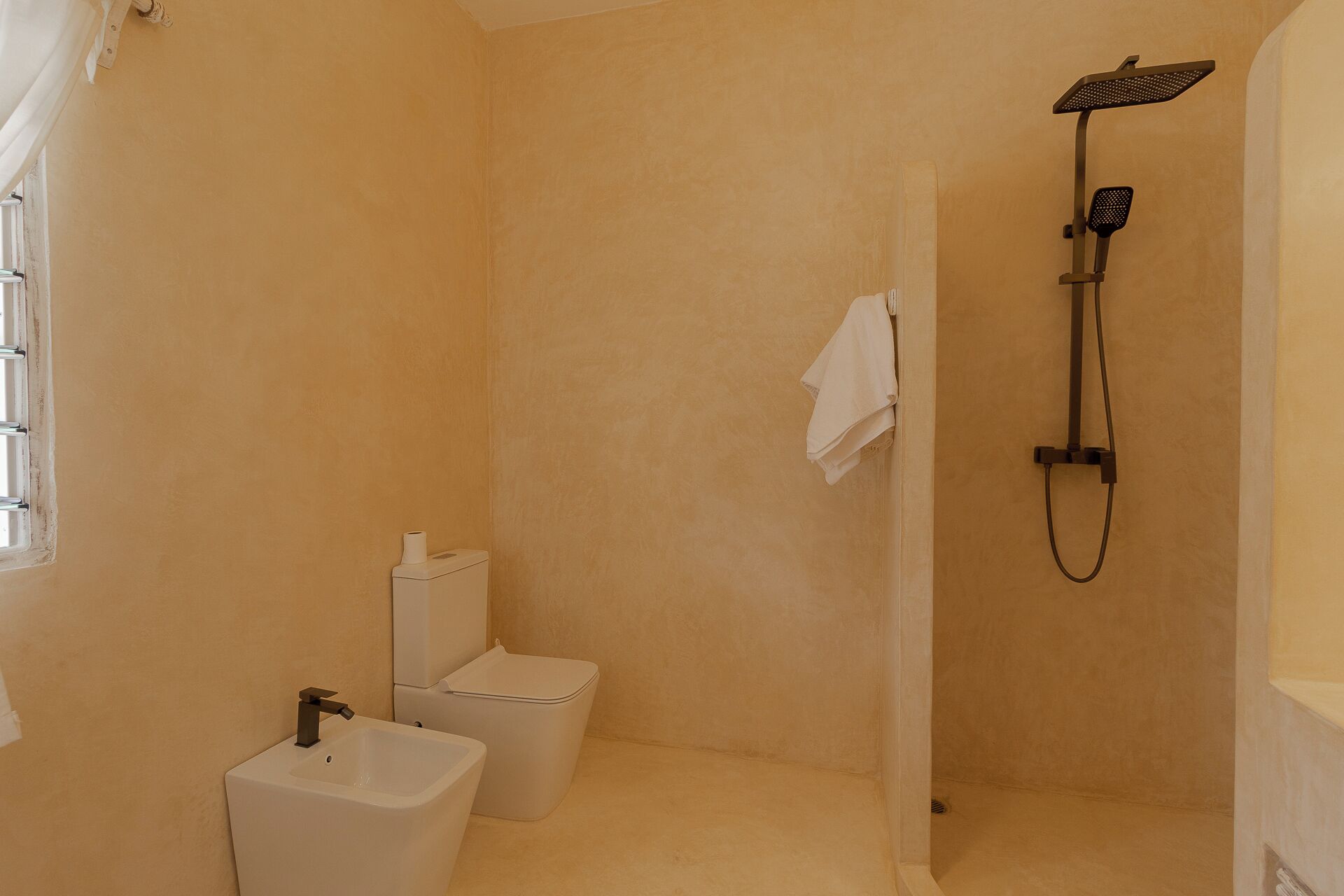 A small, single-bathroom with a toilet, bidet, and shower.