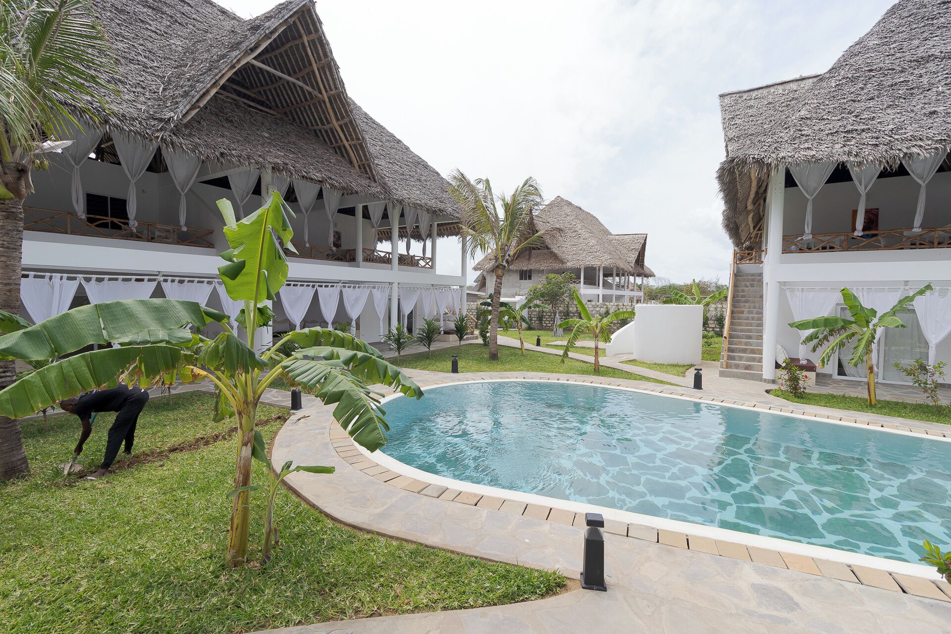A resort with thatched-roof villas, a swimming pool, and lush greenery.
