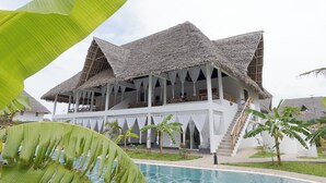 A resort with a pool, thatched-roof structures, and a white building with balconies. - Ndoto House in Rafiki Tamu Dunia Resort (Watamu)