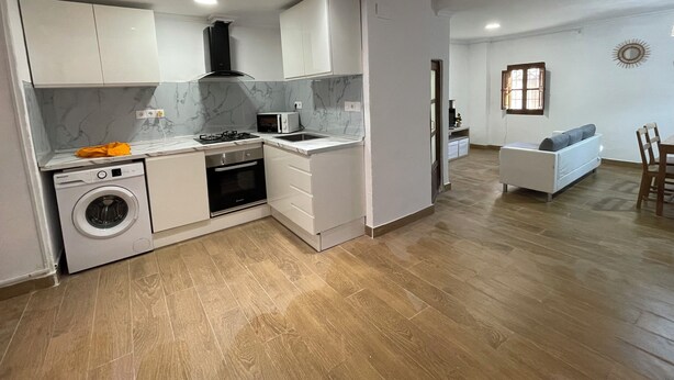 A modern kitchen with built-in appliances, a washing machine, and a dining area with a sofa and table. - House with terrace and views. Brand new in the middle of nature (Chelva)