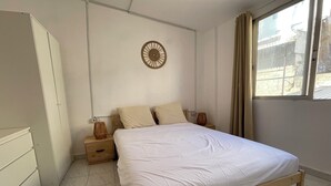 A bedroom with a wooden bed, a bedside table with a lamp, a wall clock, and a window with curtains. - House with terrace and views. Brand new in the middle of nature (Chelva)