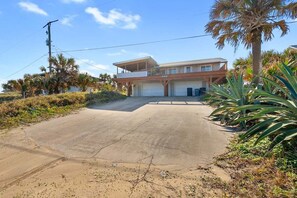 A two-story house with a garage, surrounded by palm trees and a concrete driveway.