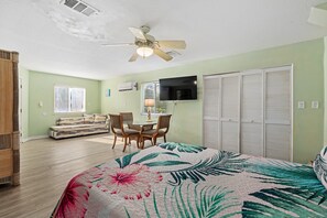 Une chambre à coucher comprenant un lit, un ventilateur de plafond, une télévision, un canapé et une table à manger avec des chaises.