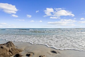 Una playa con olas, cielo despejado y algunas nubes dispersas.