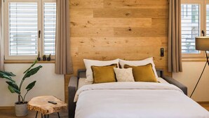 A bedroom with a wooden headboard, a bed with white bedding, a small round table with a plant, and a remote control on the table.