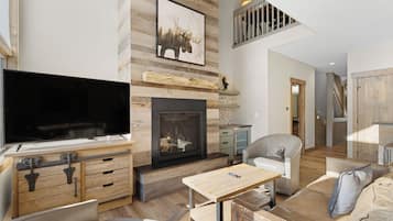 A modern living room with a fireplace, a flat-screen TV, wooden furniture, and a staircase leading to an upper level.