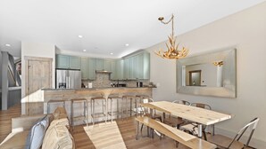 Une cuisine moderne avec des meubles de couleur vert clair, un îlot central et un coin repas comprenant une table en bois et des chaises en métal.