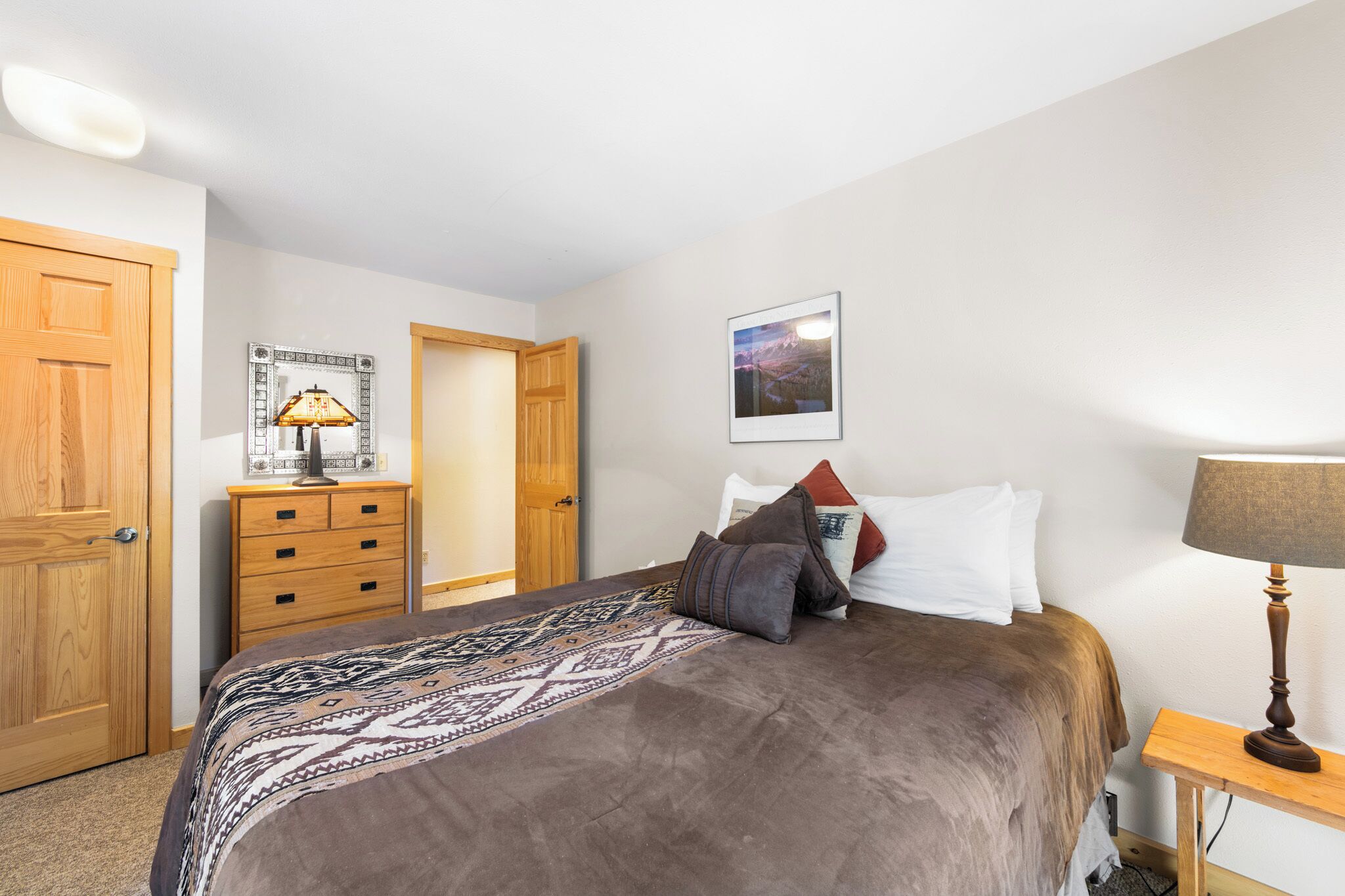 A bedroom with a bed, a wooden dresser, a lamp, and a framed picture on the wall.