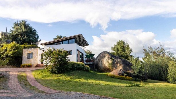 Una casa moderna con fachada de piedra, una roca grande en el jardín y cielo despejado.