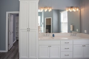 A bathroom with a double sink, white cabinets, and a large mirror with lights above. - Lakefront 6BR Retreat w Dock & Game Room (Burnet)