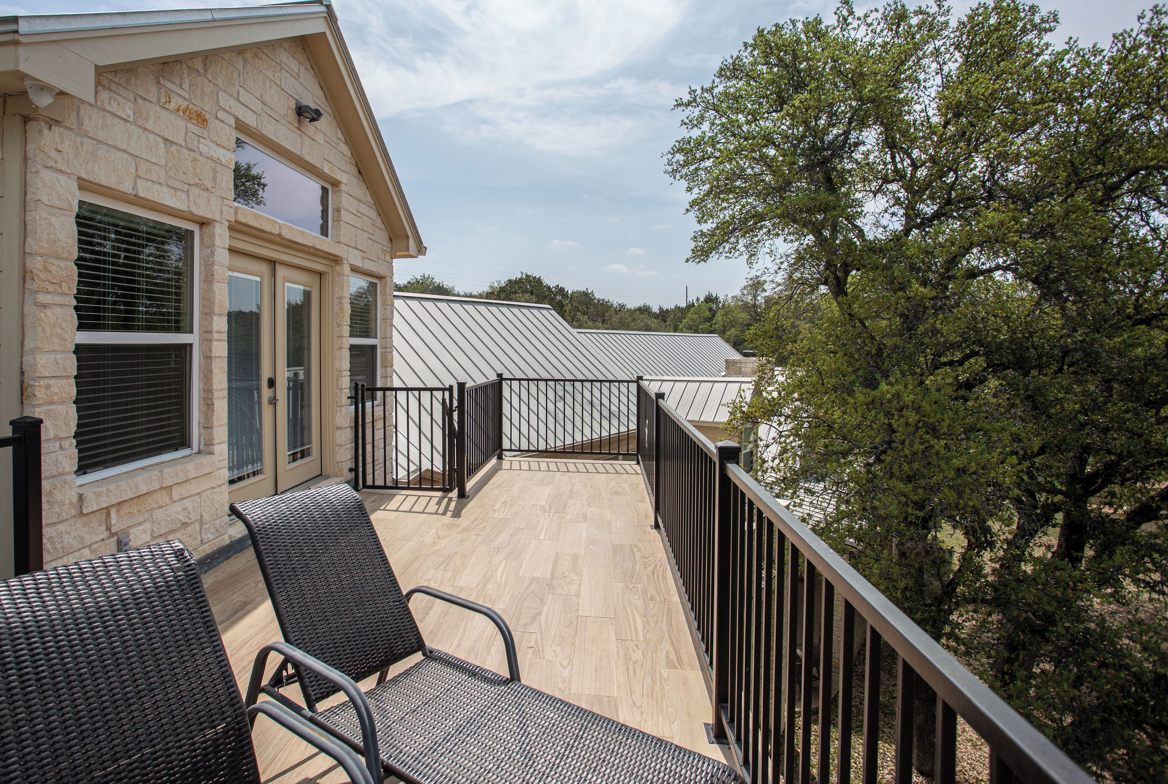 A balcony with wicker chairs, a stone building, and metal roofing.