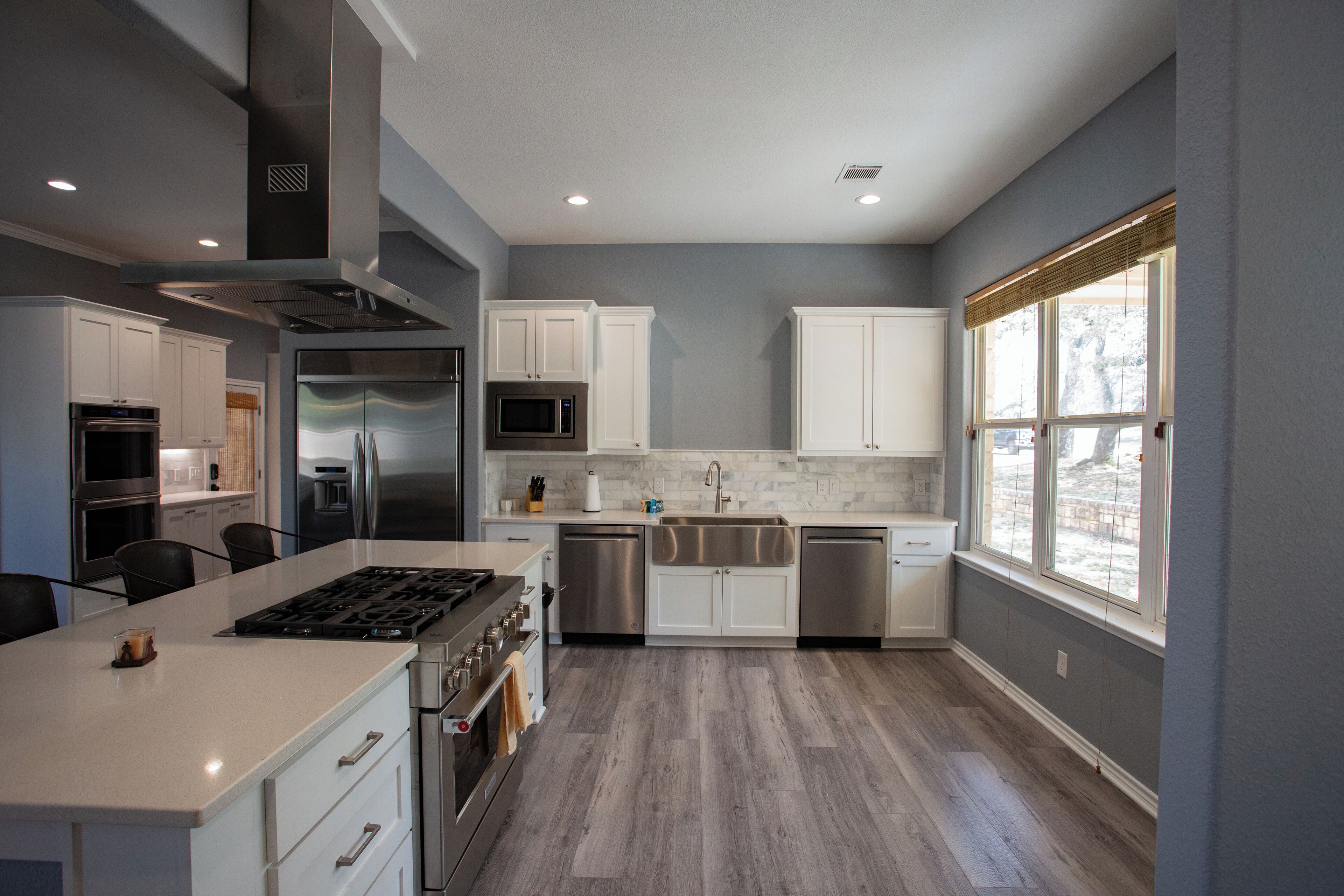 A modern kitchen with white cabinets, stainless steel appliances, and a large window providing natural light.