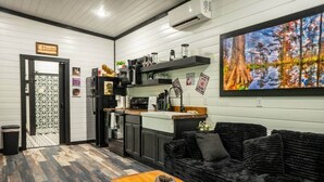 Een moderne keuken met een zwarte koelkast, een magnetron en een koffieapparaat. Er is een zwarte bank en een houten tafel met een decoratief steenobject erop.