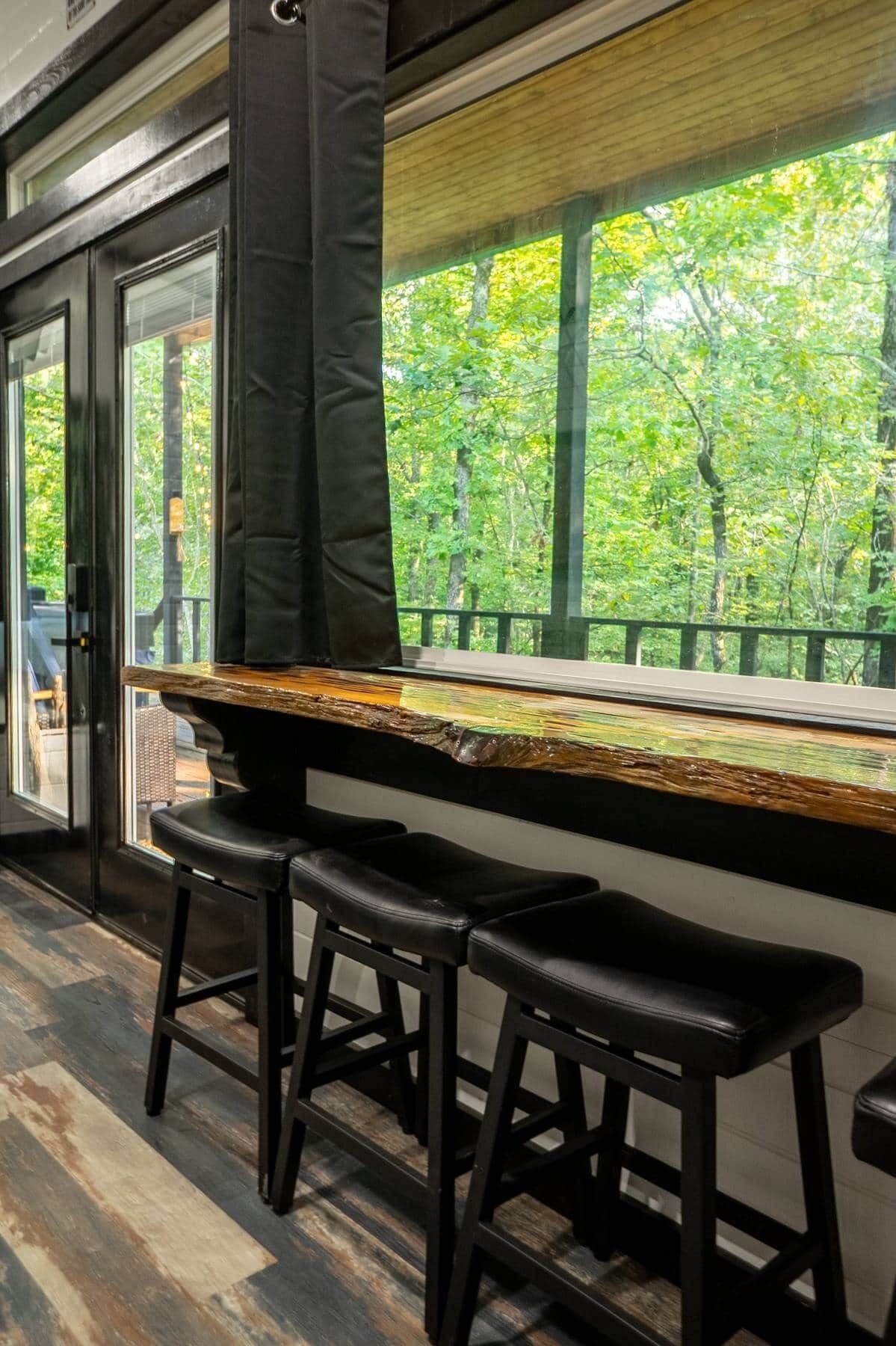 A bar area with a wooden counter and black stools.