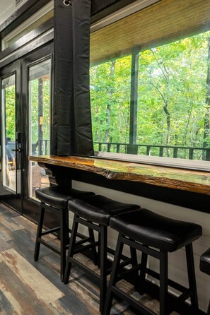 A bar area with a wooden counter and black stools.