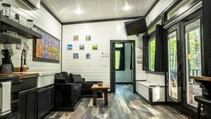 Een kamer met een bank, een tafeltje, een keukenhoek met een koffieapparaat en een wand met ingekaderde foto's.