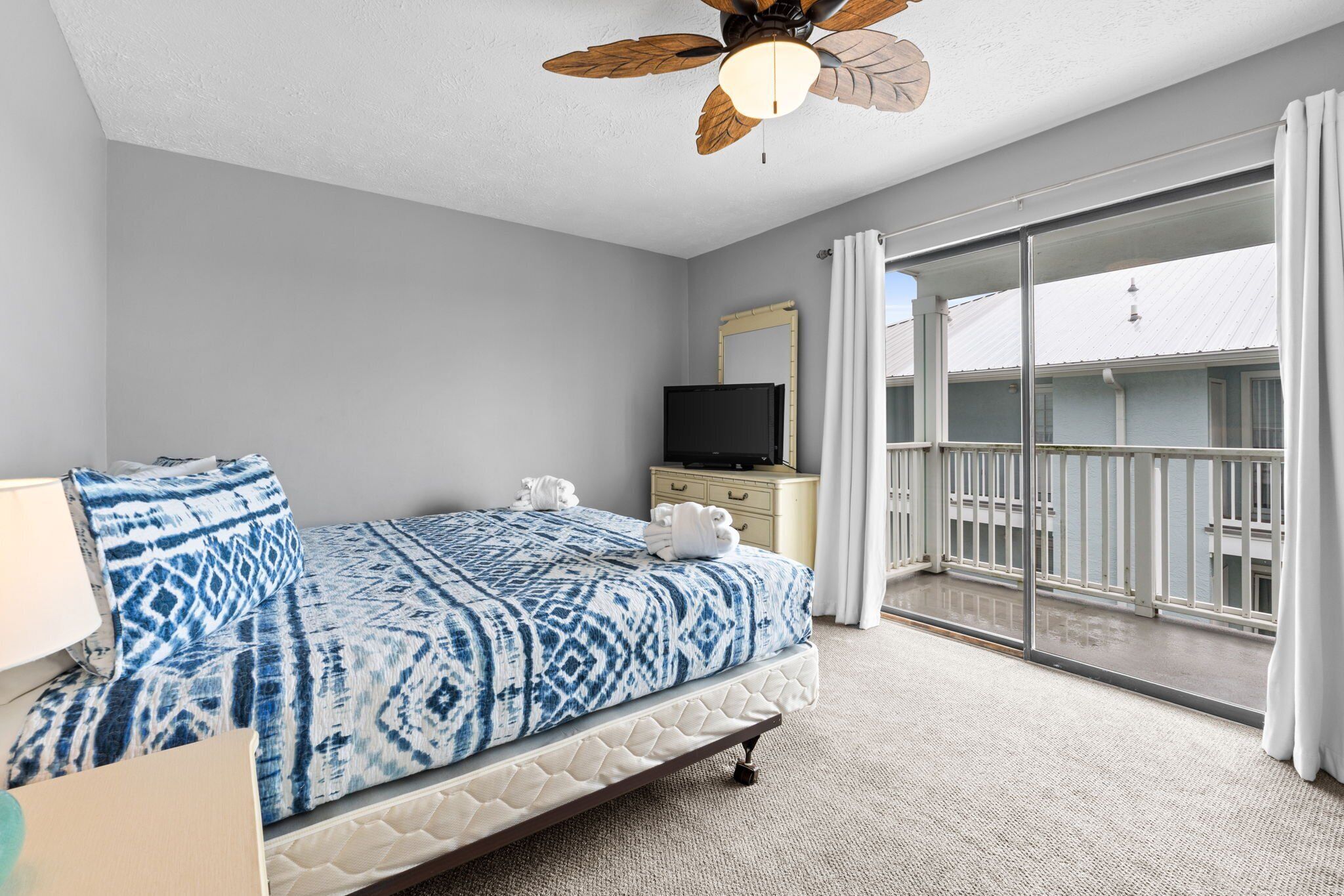 A hotel room with a bed, a TV, a balcony with a view, and a ceiling fan.