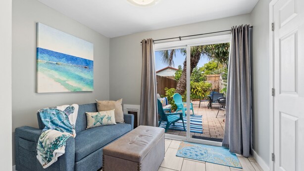 A living room with a sofa, ottoman, and a painting of a beach scene.