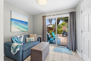 Una sala de estar con un sofá, un reposapiés y un cuadro de una playa.
